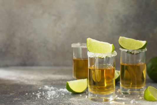 Four tequila shots with lime wedges and salt on a gray background, representing affordable tequilas worth collecting.